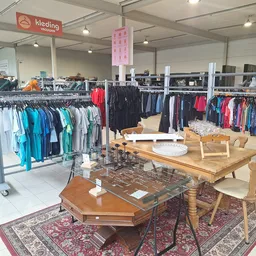 Winkelvloer met kledingrekken, houten meubels en tafels, Kleding uitgestald in turquoise, zwart en rode tinten