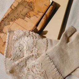 Close-up van een beige gebreide trui met witte kanten details, op een vintage kaart