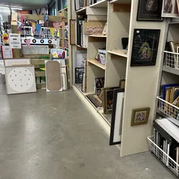 Winkelinterieur met stellingen vol boeken, ingelijste afbeeldingen aan de muur en diverse tweede-handsspullen