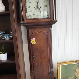 Antieke houten staande klok met glazen kast bovenaan, gele prijssticker zichtbaar