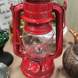 Close-up van een rode vintage campinglamp met glazen reservoir en hengsels