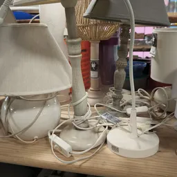 Verzameling van tweedehands tafellampjes met witte en gekleurde kapjes op een houten tafel