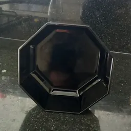 Zwart zeshoekig object met spiegelend oppervlak, mogelijk decoratief artikel of meubelstuk