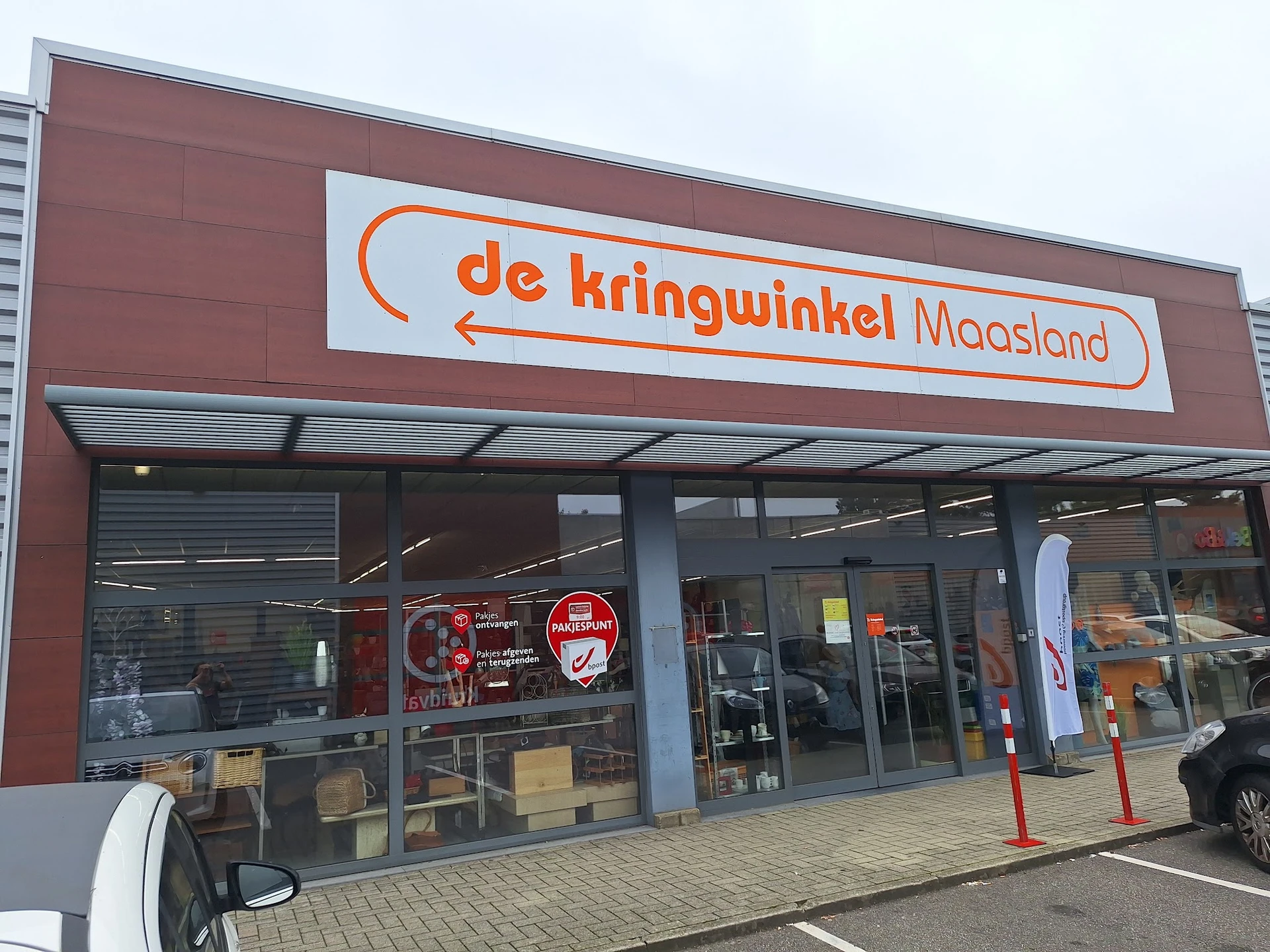 Voorgevel van kringloopwinkel met rood-bruine gevel, glazen pui en oranje logo met winzelnaam