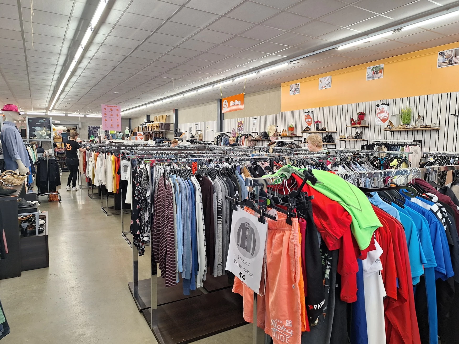 Rekken met kleding in verschillende kleuren in een kringloopwinkel