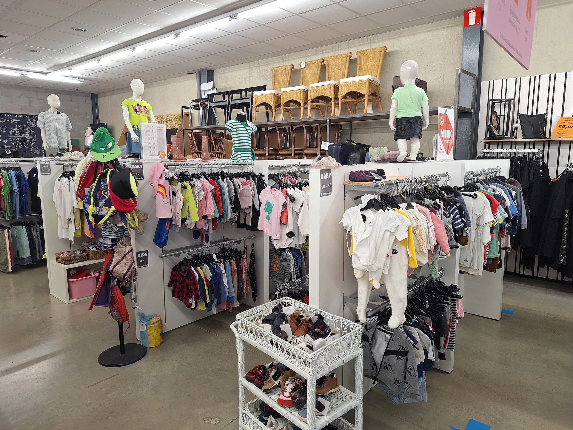 Winkelvloer met kledingrekken, mannequins en stapels tweedehands kleding in verschillende kleuren