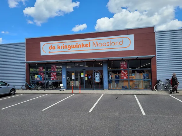 Gevel van kringloopwinkel met rode bakstenen voorgevel en daarop duidelijk zichtbare winkelnaam in oranje letters