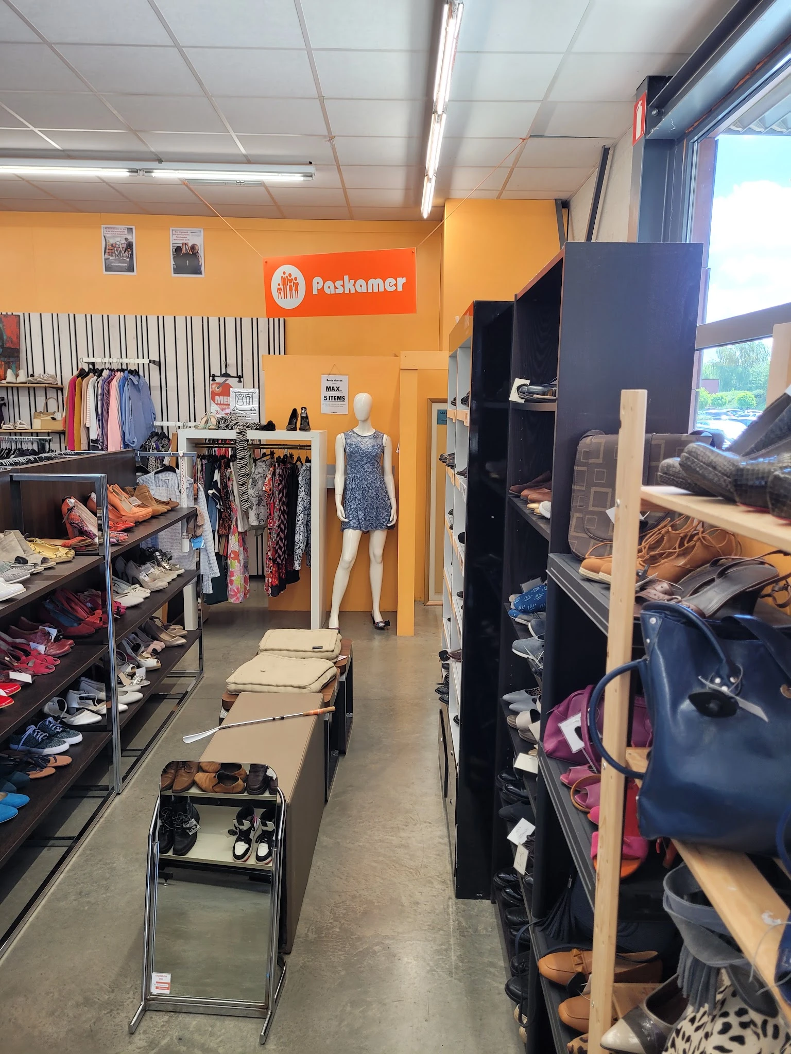 Winkelbinnenkant met oranje muur, kledingrekken, mannequin en zwarte stellingen met diverse artikelen