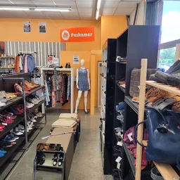 Winkelbinnenkant met oranje muur, kledingrekken, mannequin en zwarte stellingen met diverse artikelen