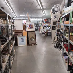 Brede winkelgang met stellingen vol tweedehands spullen, kunstwerken en decoratiestukken aan beide zijden