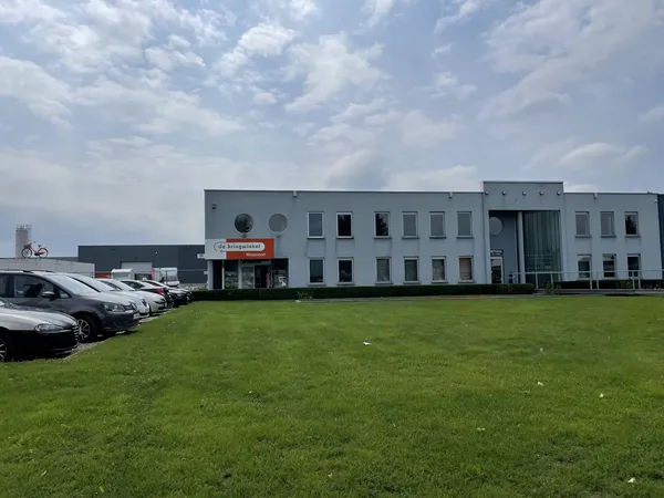 Grijze moderne gevel van kringloopwinkel met parkeerplaats en grasveld aan voorkant