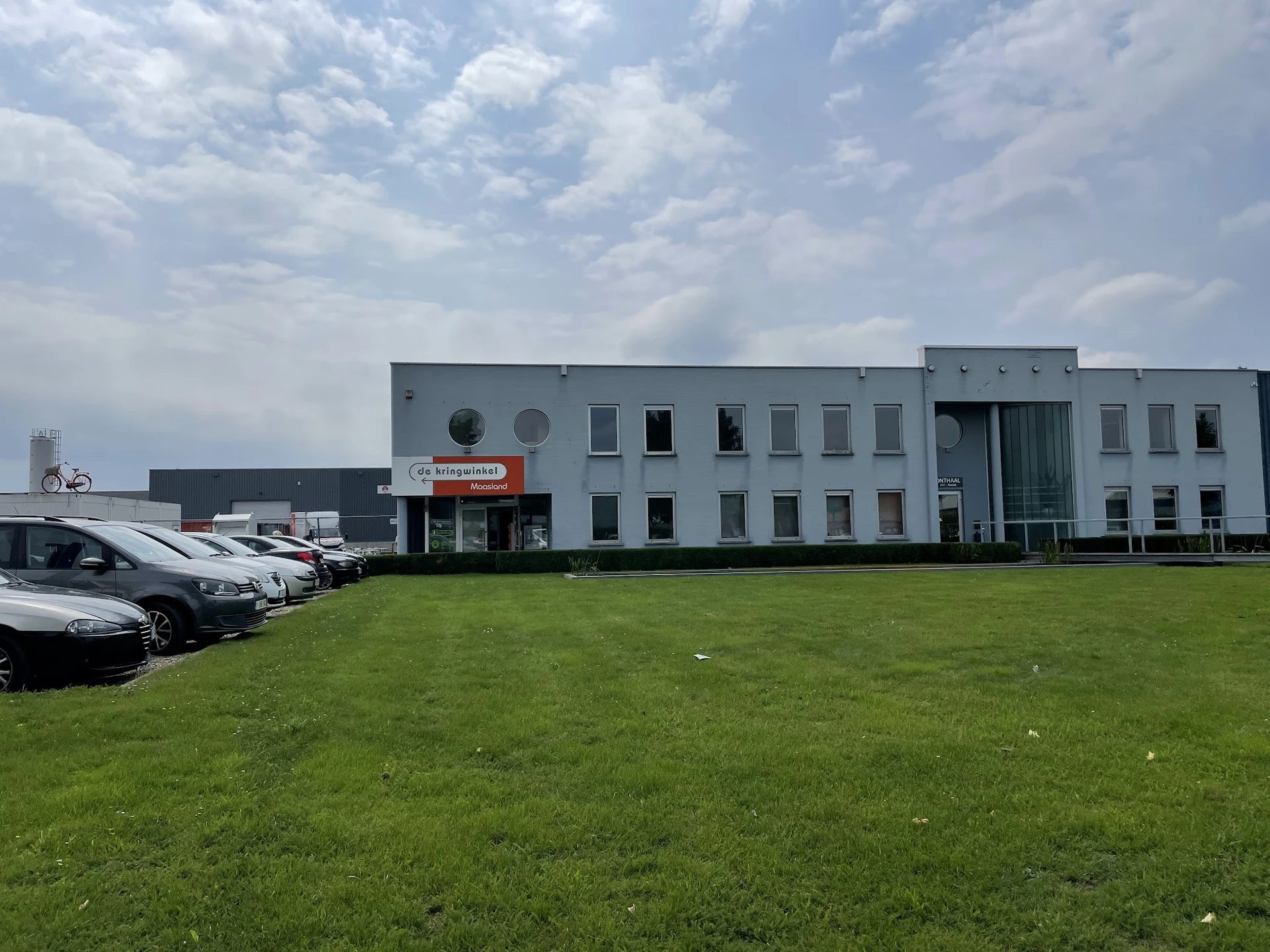 Grijze moderne gevel van kringloopwinkel met parkeerplaats en grasveld aan voorkant