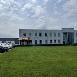 Grijze moderne gevel van kringloopwinkel met parkeerplaats en grasveld aan voorkant