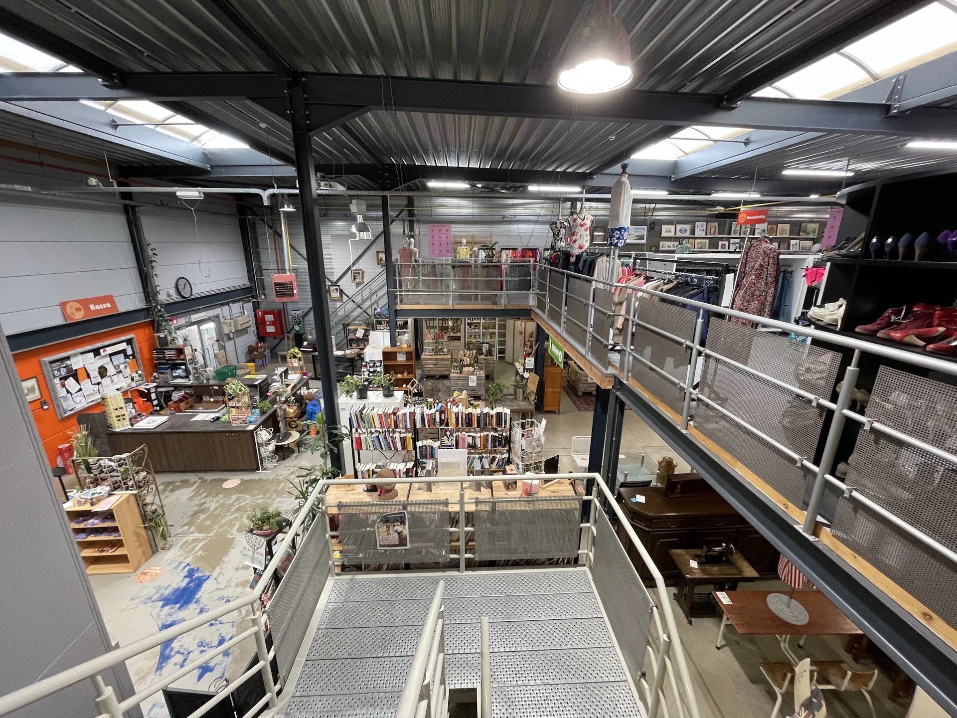 Overzicht van een kringloopwinkel met meerdere verdiepingen, stellingen met tweedehands spullen en diverse artikelen