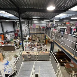 Overzicht van een kringloopwinkel met meerdere verdiepingen, stellingen met tweedehands spullen en diverse artikelen