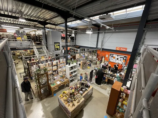 Overzicht van de winkelvloer met verschillende afdelingen, stellingen en uitgestalde spullen in een kringloopwinkel