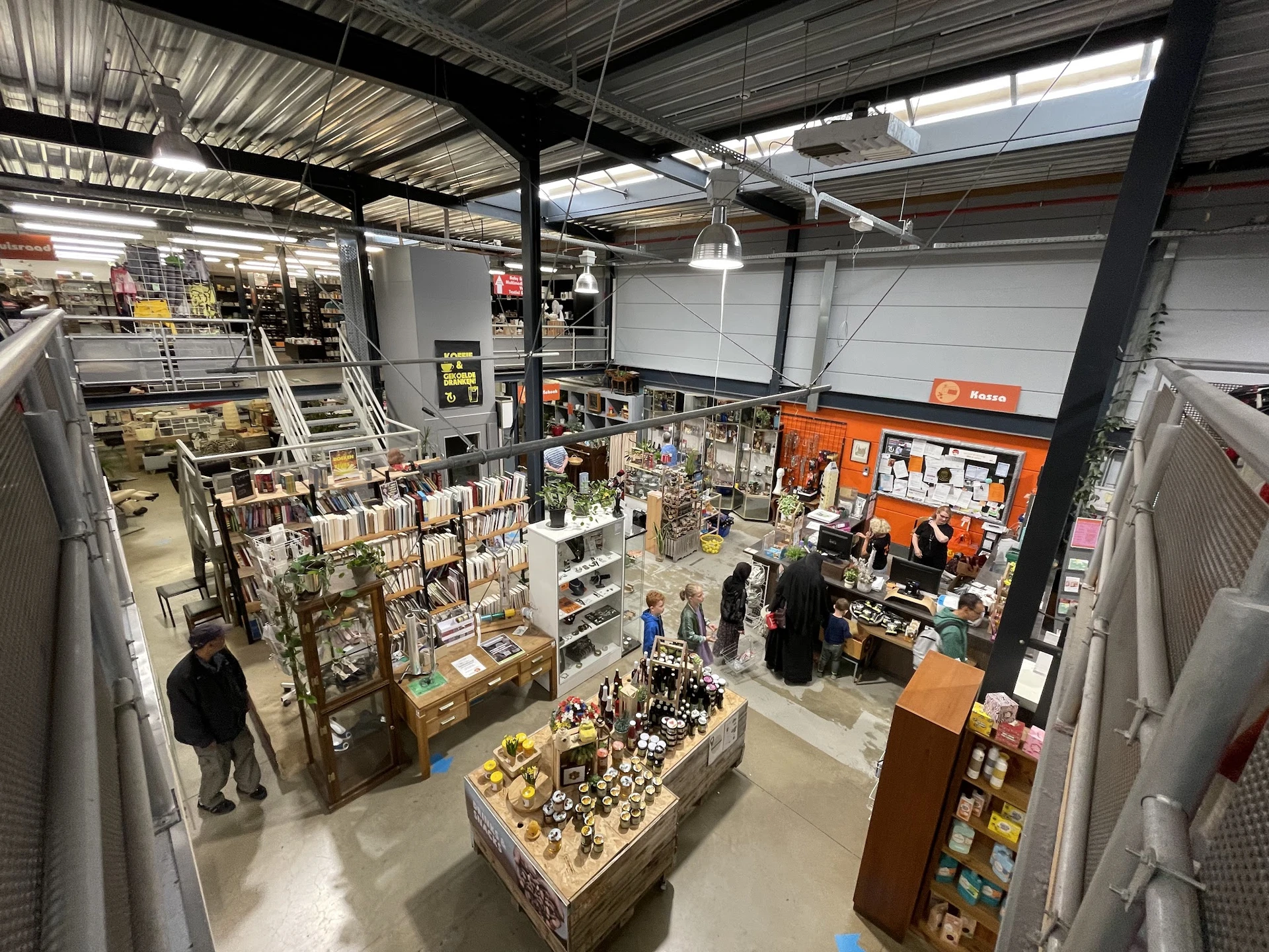 Overzicht van de winkelvloer met verschillende afdelingen, stellingen en uitgestalde spullen in een kringloopwinkel