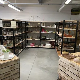 Winkelinterieur met zwarte stellingen vol met spullen, houten toonbanken aan beide zijden en heldere verlichting
