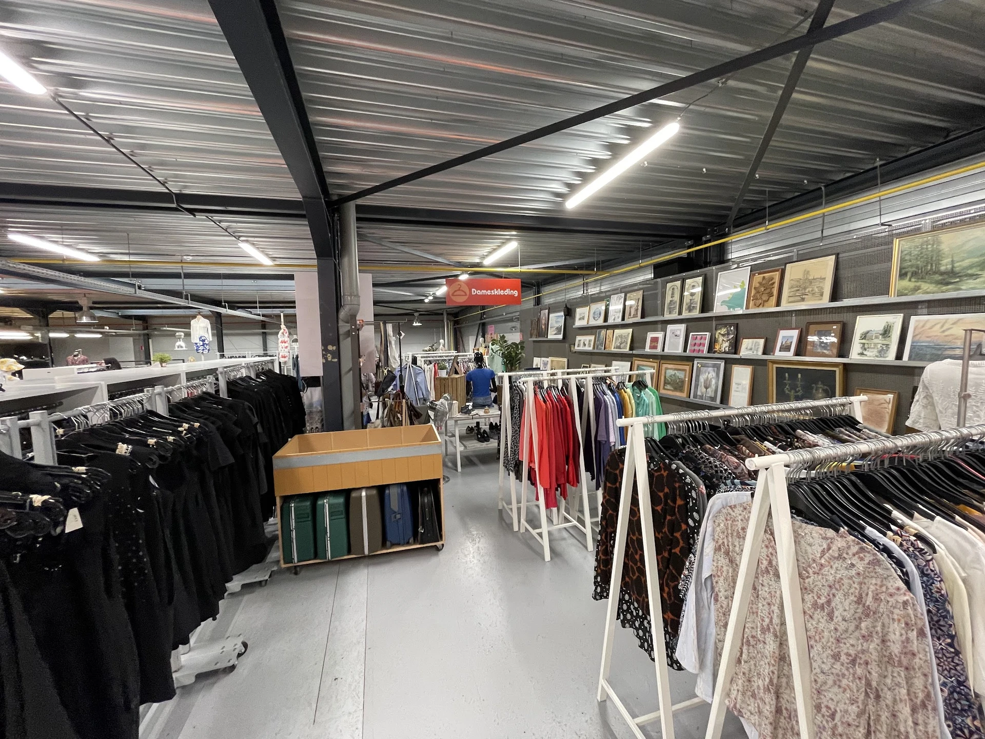 Overzicht van de winkelruimte met kledingrekken, stellingen met artikelen en decoratieve items aan de wand