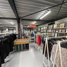 Overzicht van de winkelruimte met kledingrekken, stellingen met artikelen en decoratieve items aan de wand