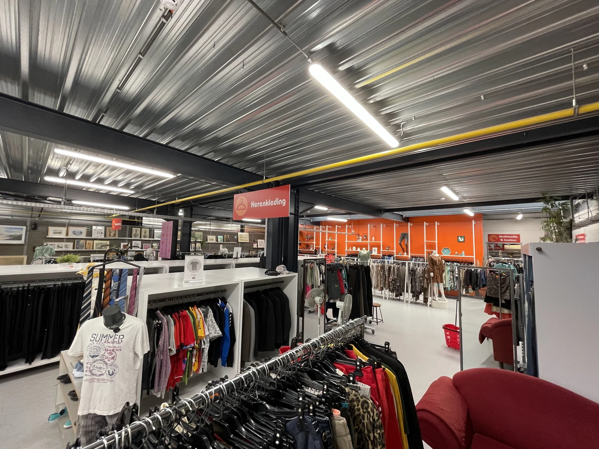 Ruim winkelinterieur met kledingrekken, verlichte plafondpanelen en oranje wanddecoraties