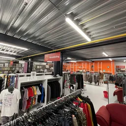 Ruim winkelinterieur met kledingrekken, verlichte plafondpanelen en oranje wanddecoraties