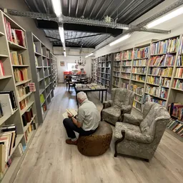 Leesgedeelte in kringwinkel met boekenkasten, leunstoel en man die leest