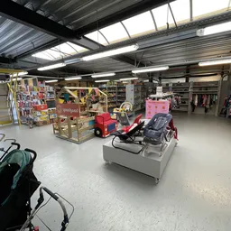 Ruime winkelhal met stellingen, kleding aan rekken, speelgoed en diverse spullen op tafels