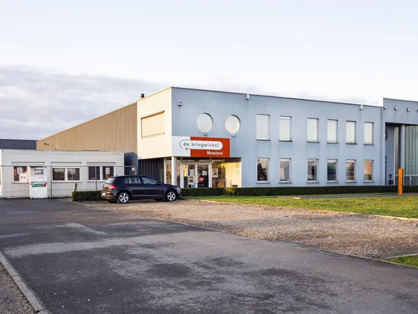 Gevel van kringloopwinkel met geel en blauw geverfd pand, parkeerplaats met auto aan voorkant