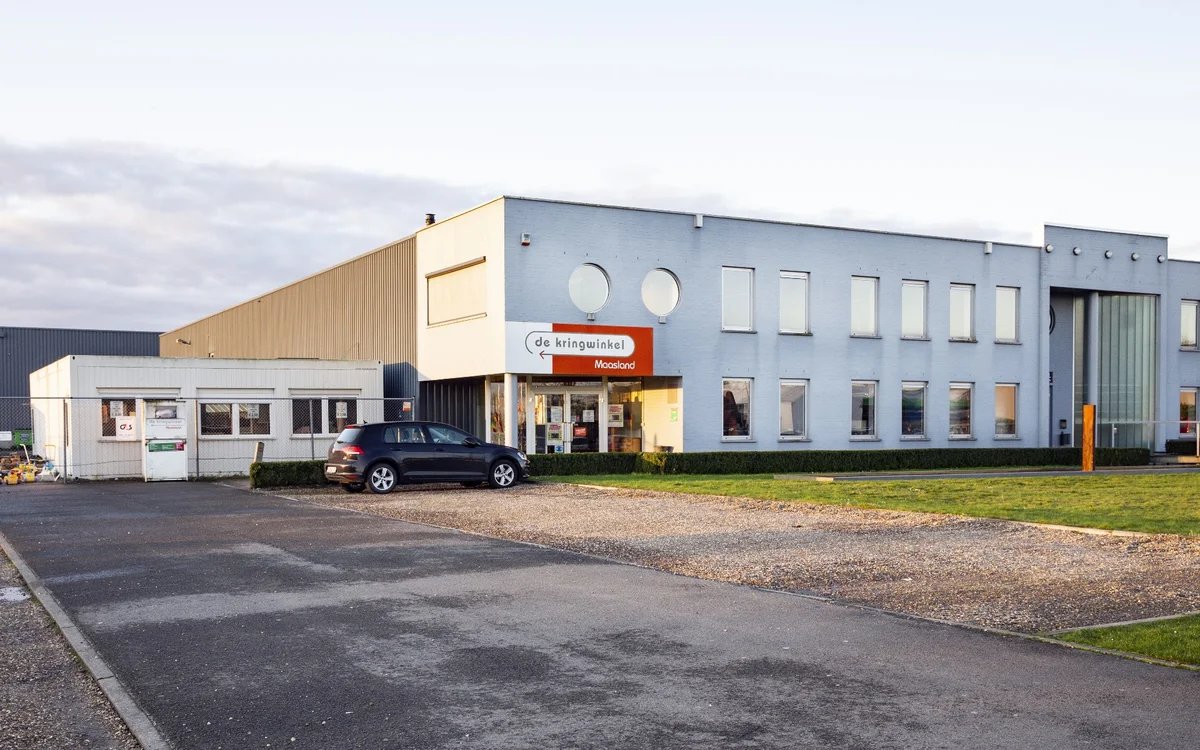 Gevel van kringloopwinkel met geel en blauw geverfd pand, parkeerplaats met auto aan voorkant