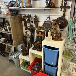 Stellingen met religieuze beelden, kruisen, vazen en decoratieve objecten in tweedehands winkel