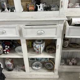 Witte kastenwand met openrekken vol decoratief serviesgoed, porseleinen vazen en borden