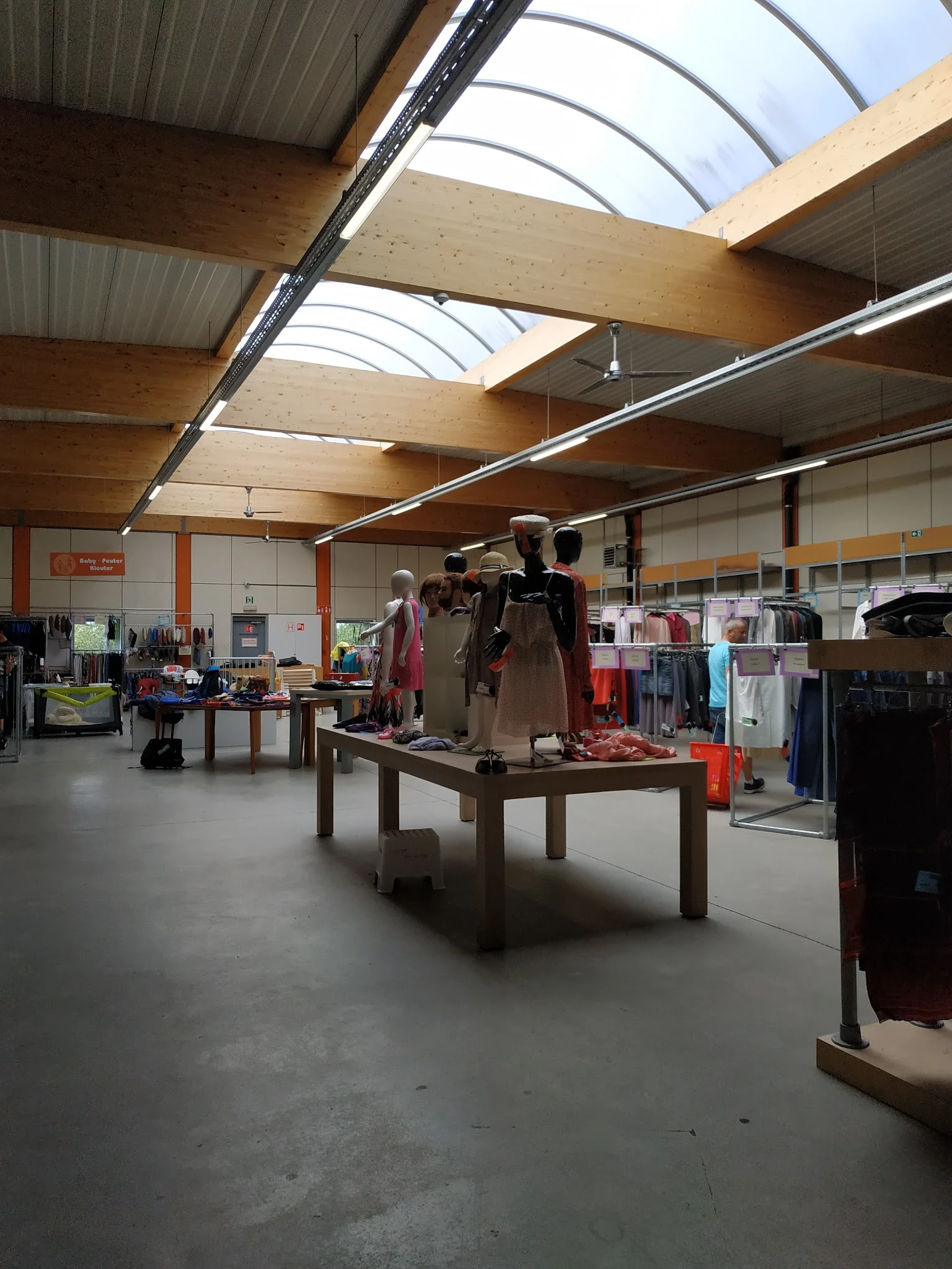 Winkelvloer met kledingrekken, tafels met uitgestalde kleding en mannequins in een ruime hal met houten dakconstructie