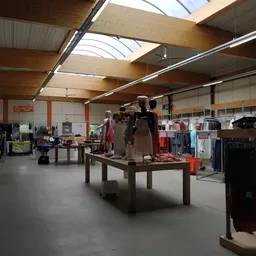 Winkelvloer met kledingrekken, tafels met uitgestalde kleding en mannequins in een ruime hal met houten dakconstructie