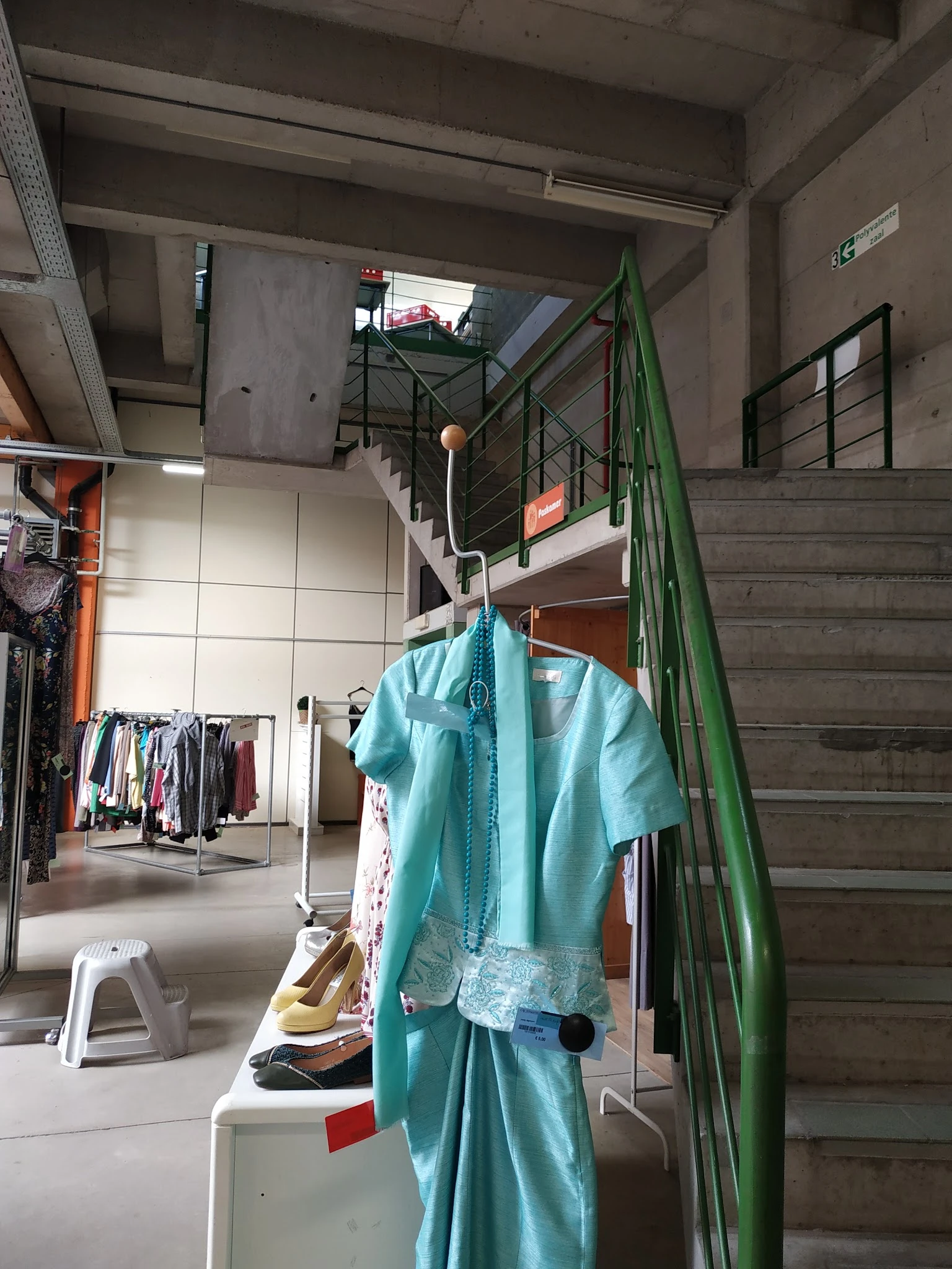 Turquoise blouse aan hangers tussen rekken met tweedehands kleding in de winkel