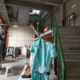 Turquoise blouse aan hangers tussen rekken met tweedehands kleding in de winkel