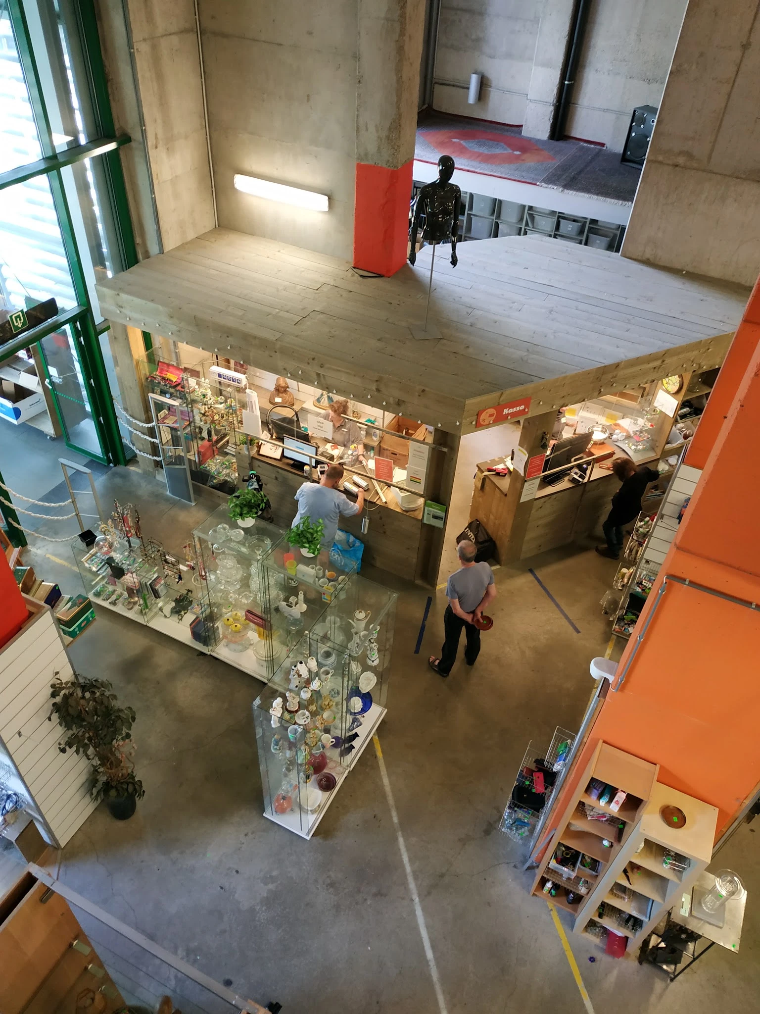 Overzicht van een kringloopwinkel met vitrines, stellingen en bezoekers op de winkelvloer