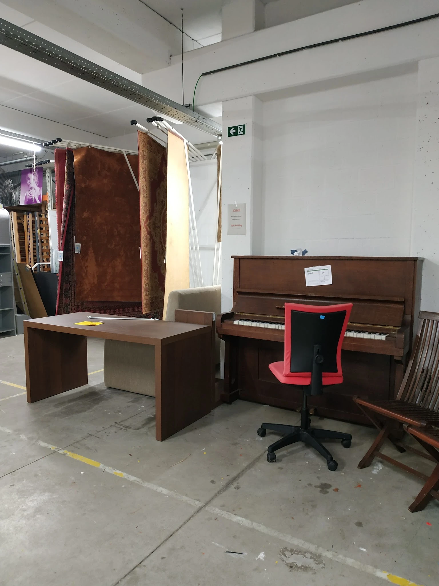 Bruine houten meubels in de winkel: een bureau, een piano en een rode bureaustoel