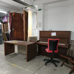 Bruine houten meubels in de winkel: een bureau, een piano en een rode bureaustoel