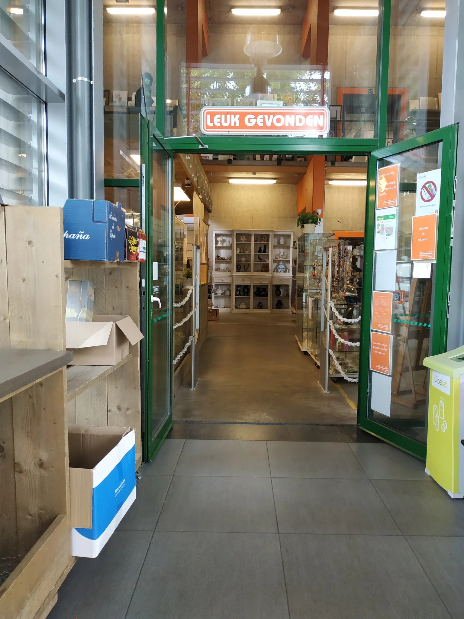 Winkelinterieur met groene deuringang, houten stellingen met spullen en oranje muren