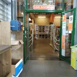 Winkelinterieur met groene deuringang, houten stellingen met spullen en oranje muren