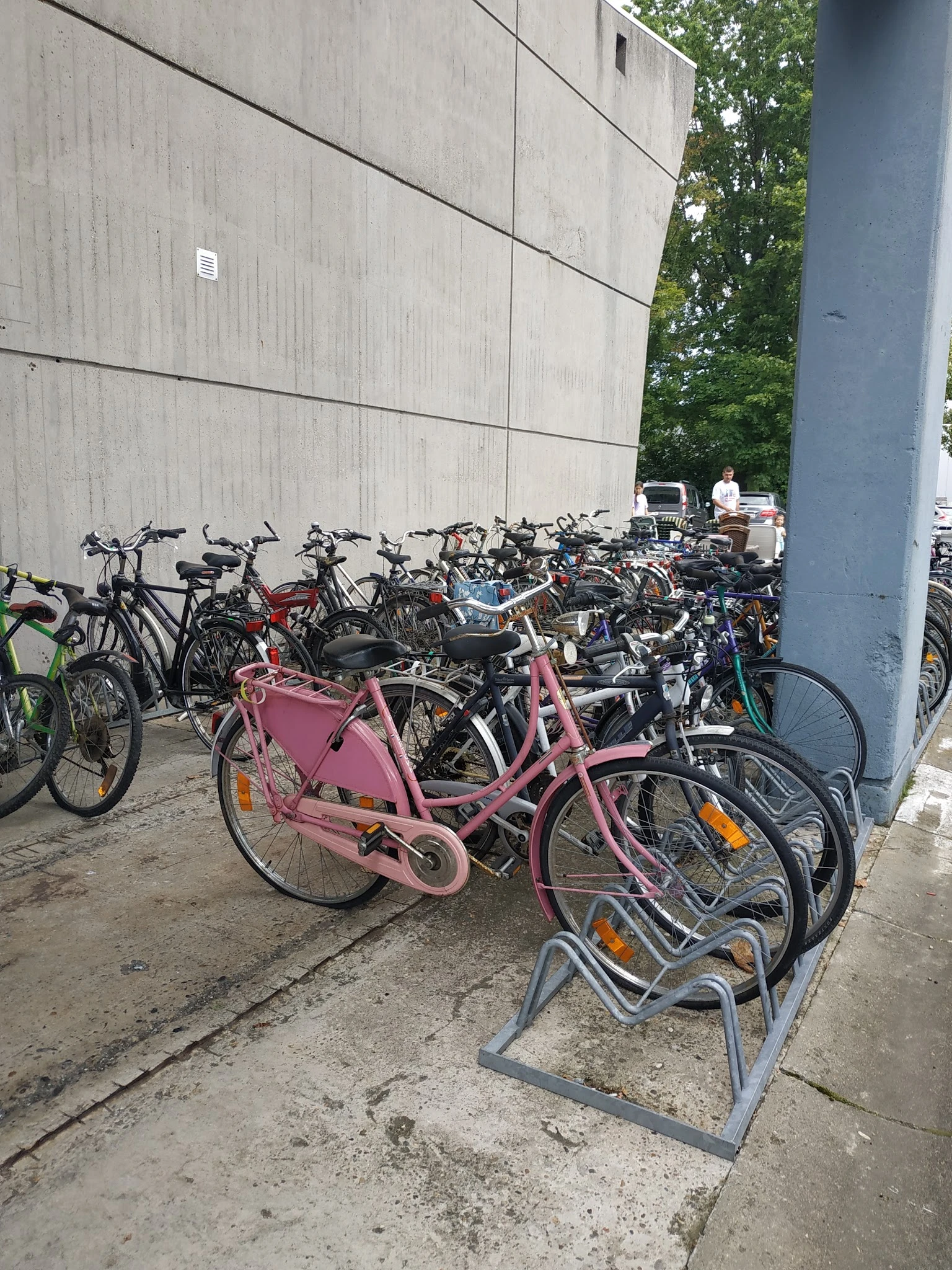 Verzameling tweedehands fietsen buiten tegen een betonnen wand, waaronder roze damesfiets op de voorgrond