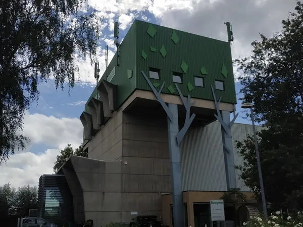Opvallend groen modern gebouw met grote openingen, omgeven door bomen