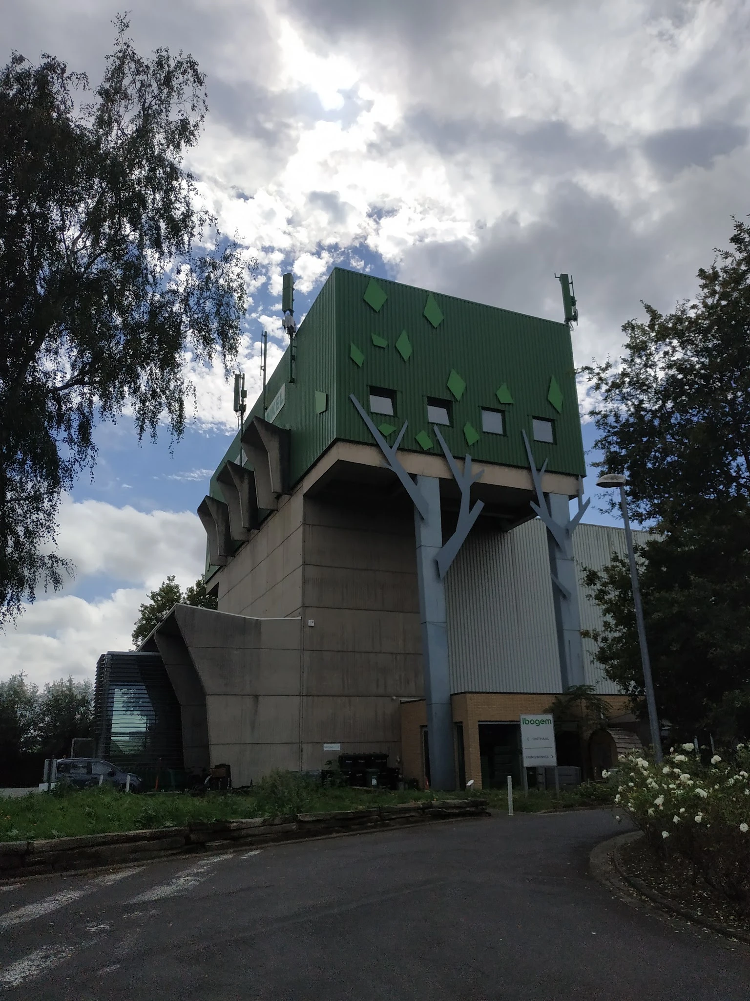 Opvallend groen modern gebouw met grote openingen, omgeven door bomen