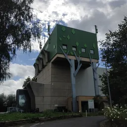 Opvallend groen modern gebouw met grote openingen, omgeven door bomen