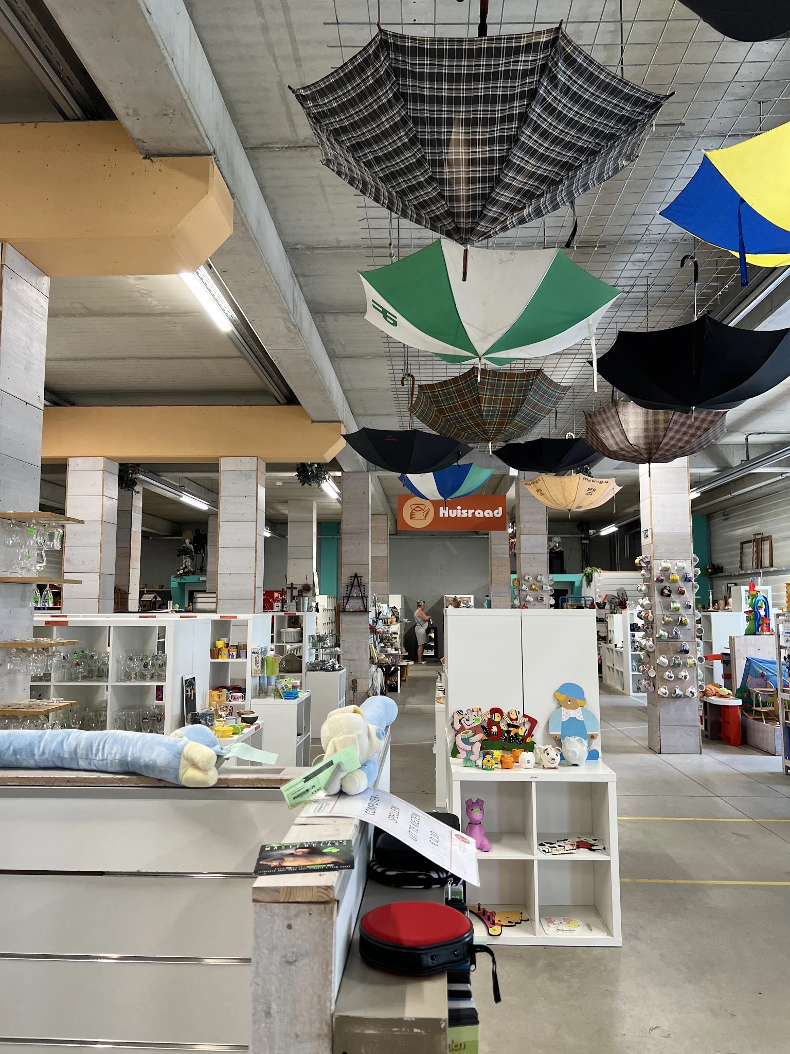 Ruim winkelinterieur met witte stellingen vol huishoudartikelen en decoratie, gekleurde paraplu's aan het plafond