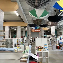 Ruim winkelinterieur met witte stellingen vol huishoudartikelen en decoratie, gekleurde paraplu's aan het plafond