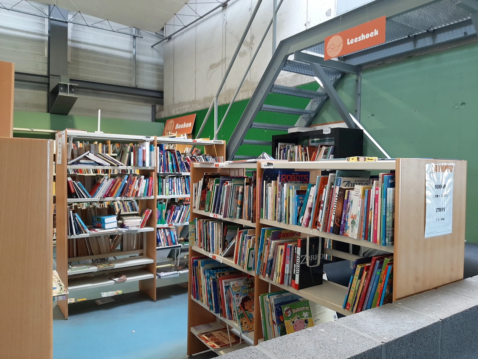 Boekenkasten met tweedehands boeken in een kringloopwinkel, met groene muren en industriële plafondstructuur