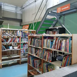 Boekenkasten met tweedehands boeken in een kringloopwinkel, met groene muren en industriële plafondstructuur