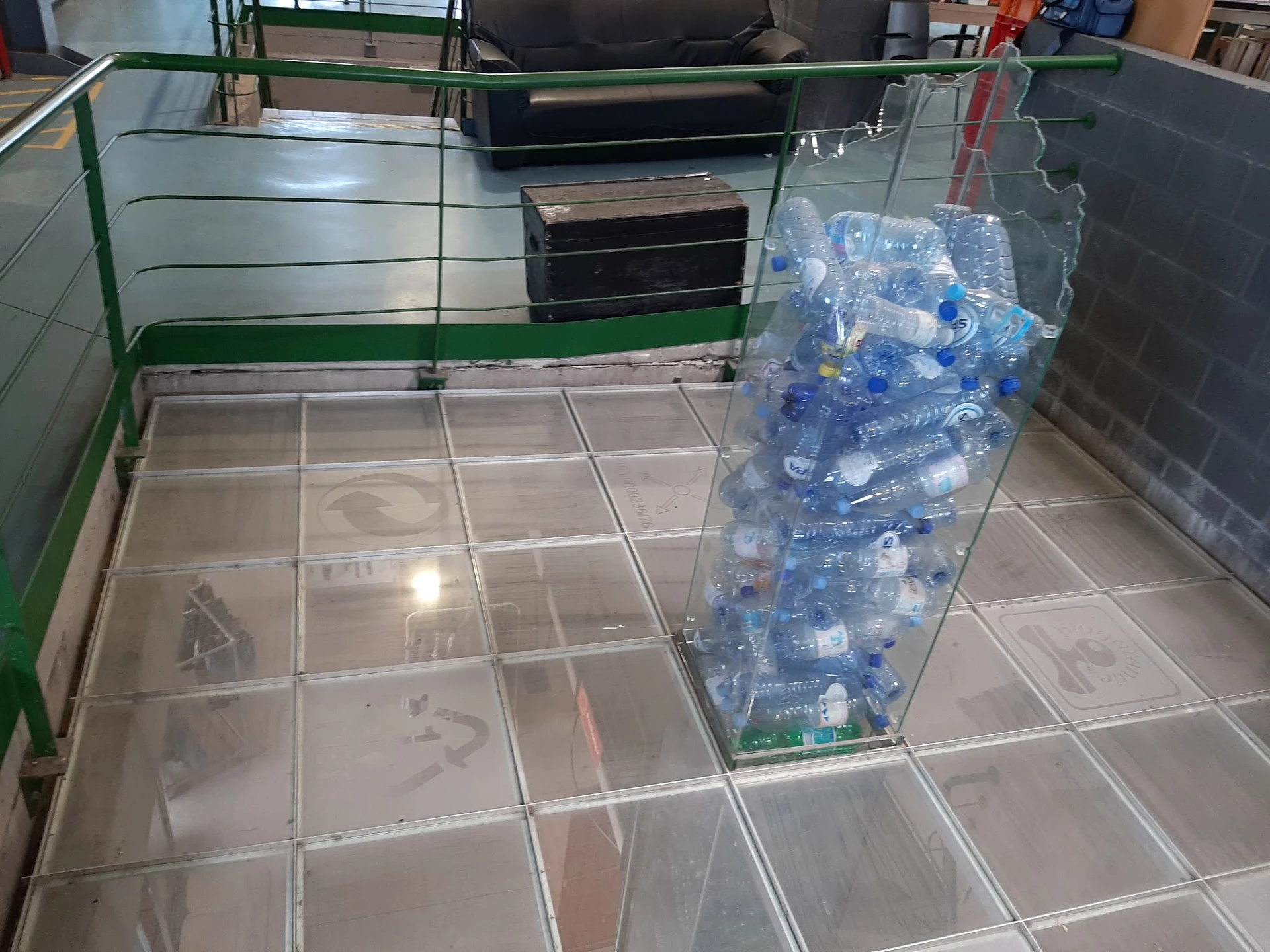 Winkelvloer met tegel, grote bak vol plastic flessen voor recycling, en zwarte dozen op achtergrond